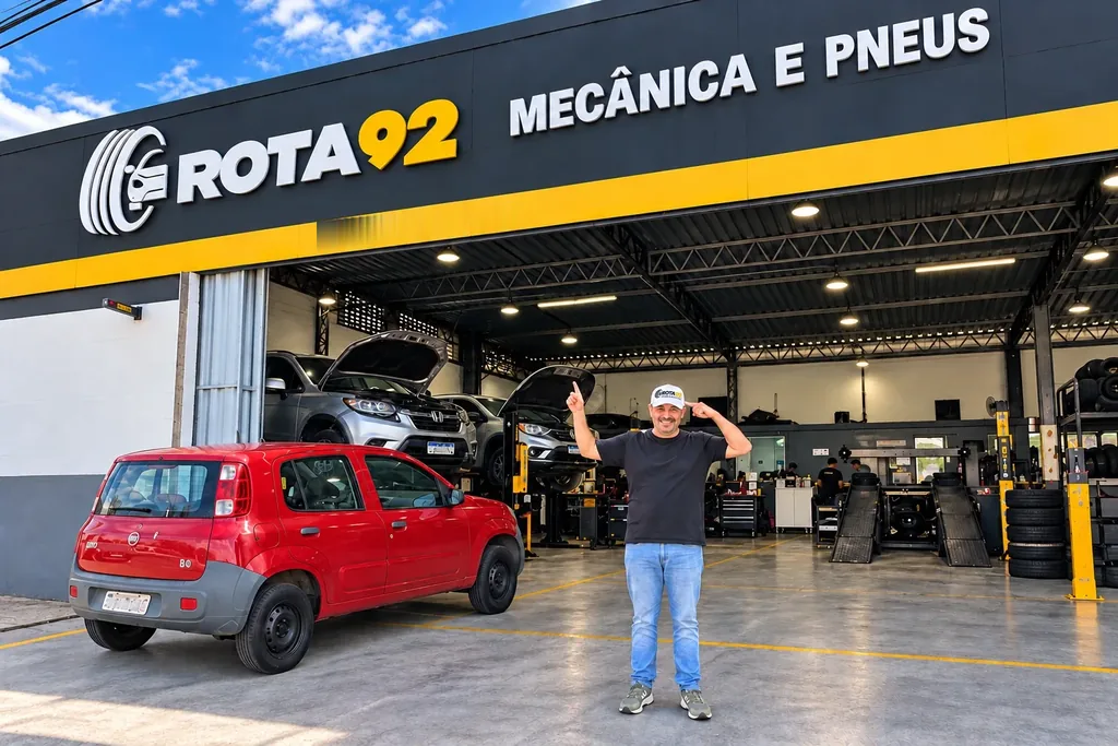 Luiz em frente à fachada do Rota 92, com a oficina e os veículos ao fundo